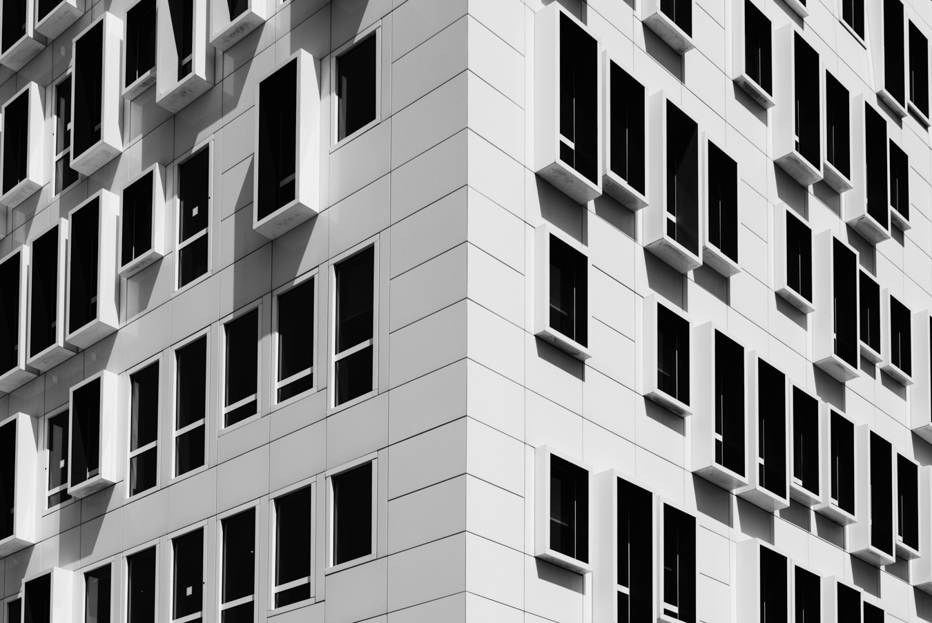 Cette photo en noir et blanc montre une façade d'immeuble à Marseille. Les lignes et les motifs géométriques donnent une impression de profondeur et de texture à la surface lisse de la façade.